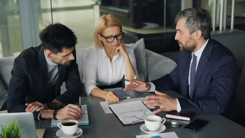 Três profissionais em reunião analisando gráficos impressos sobre a mesa