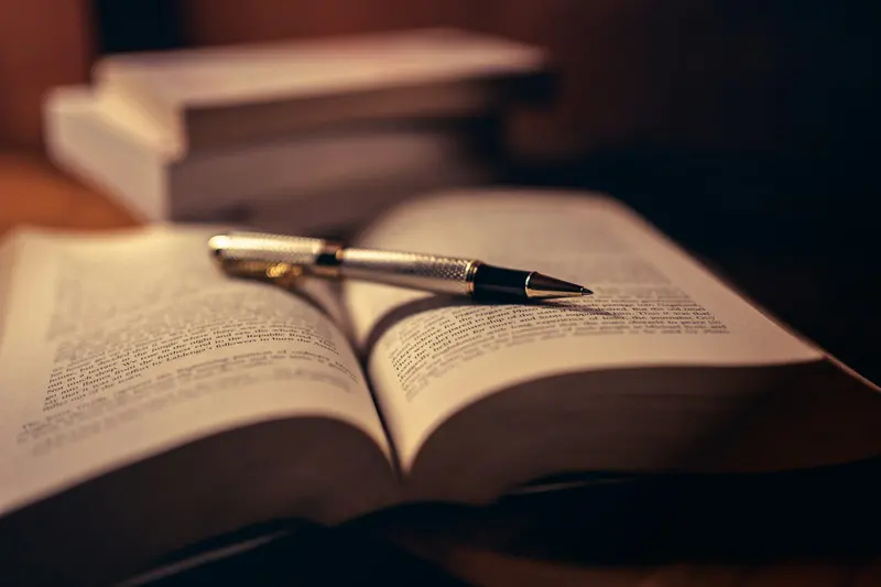 Caneta prateada apoiada sobre um livro aberto, com pouca luz